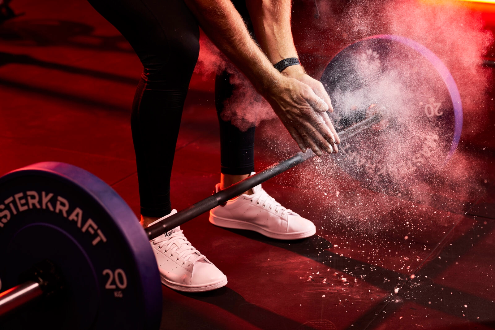 Lifter chalking up over a MasterKraft barbell loaded with 20 kg bumper plates