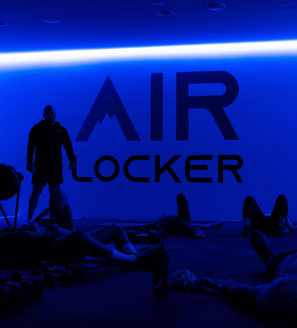 Class stretching out on the floor of a blue-lit studio under an Air Locker wall graphic