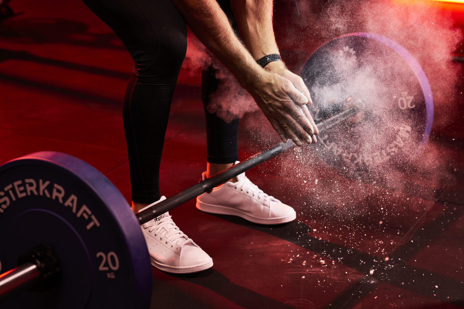 Lifter chalking up over a MasterKraft barbell loaded with 20 kg bumper plates