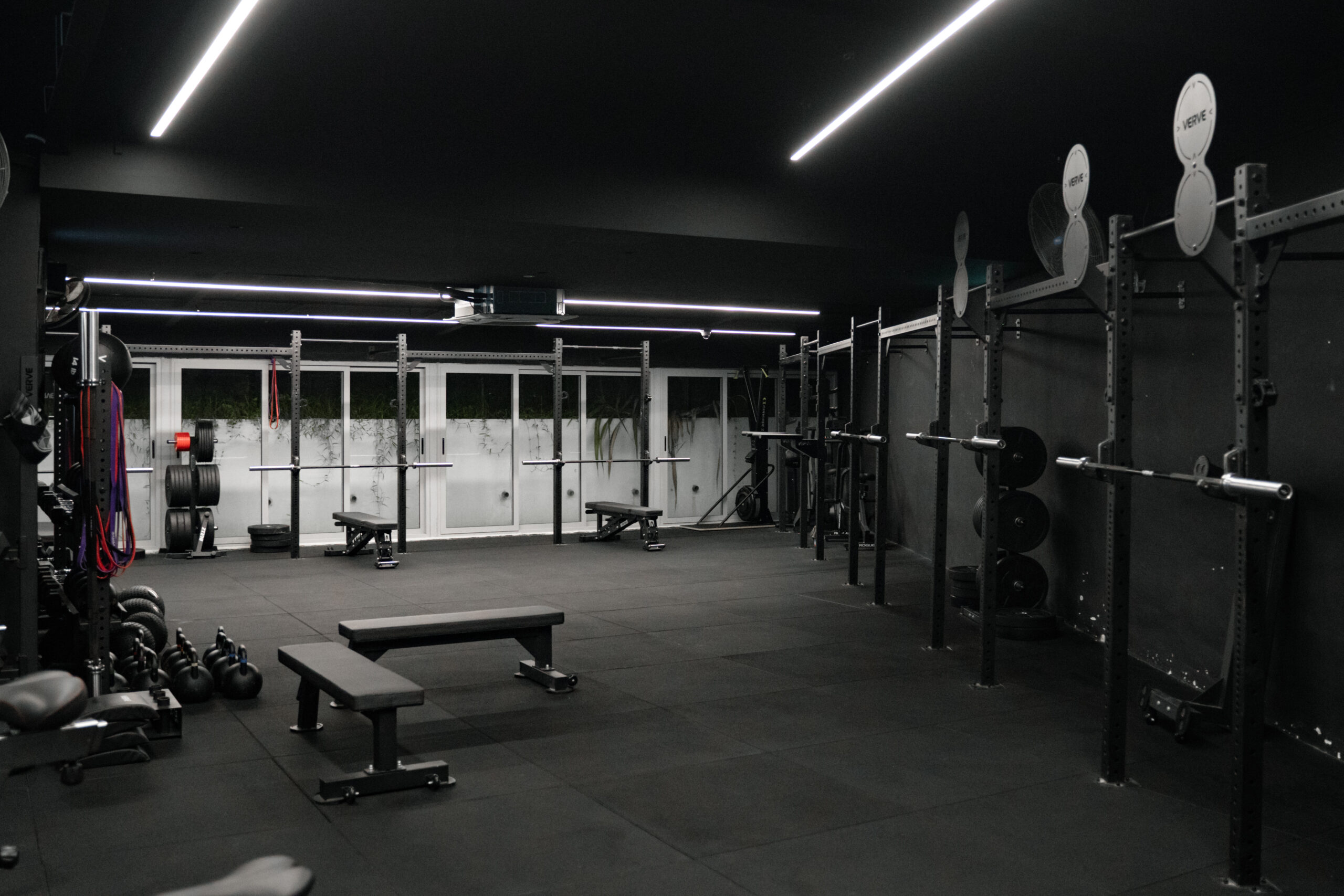 Rig, benches, kettlebells and plate storage on the floor of a blacked-out training studio